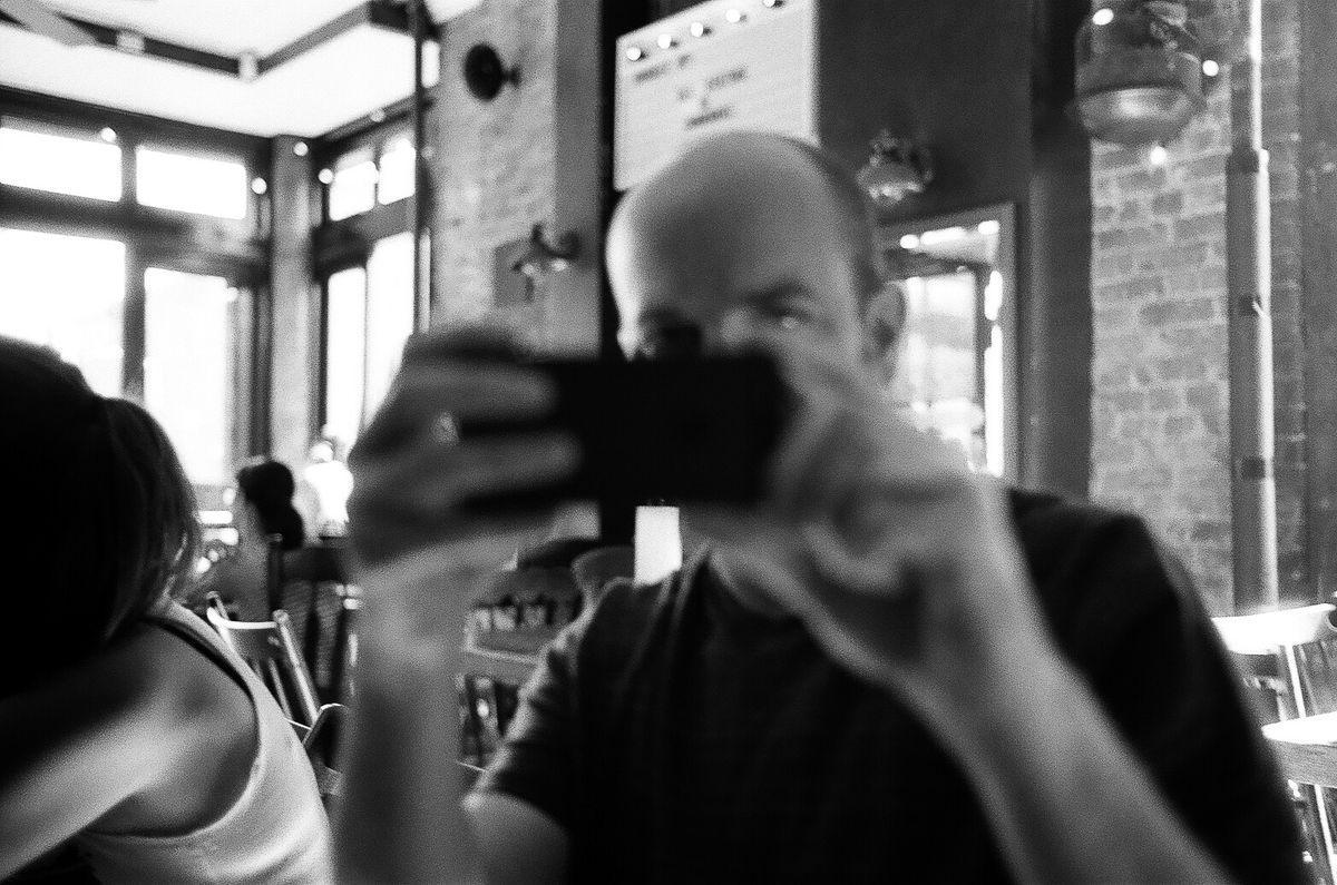 A blurry photo of the author, sitting in a bar, holding an iphone up to his face. 