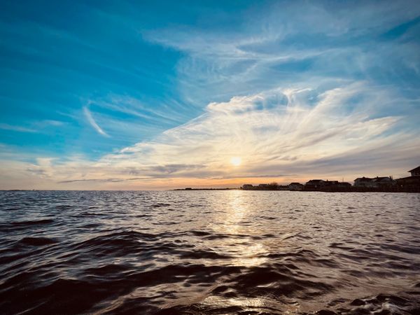 A sunset over the water with a big blue sky and clouds.